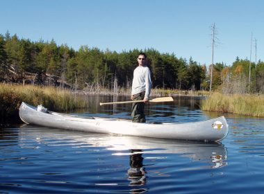 Man standing in canoe on river. A\J AlternativesJournal.ca