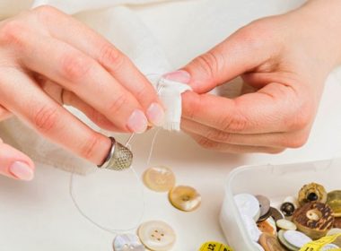 (Photo: a woman sews a button on fabric)